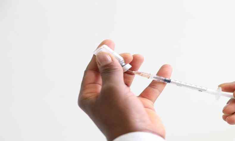 Mãos de profissional de saúde com um frasco de vacina e uma seringa