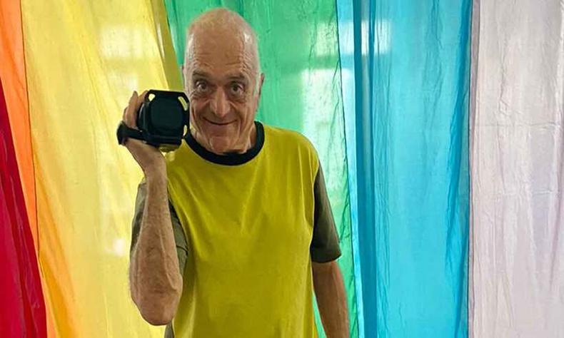 Diretor Philippe Vallois sorri e segura a cmera, tendo ao fundo bandeira com as cores do movimento LGBT 
