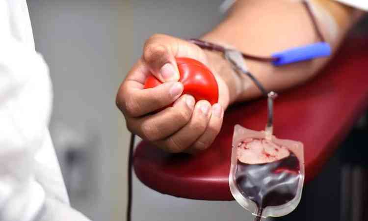 imagem com foco no brao de um homem doando sangue e segurando uma bolinha