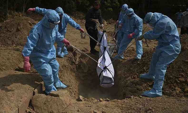 Familiares usando equipamentos de proteo individual para sepultar vtima da COVID-19 em Nova Delhi, na ndia, no fim de abril(foto: Tauseff Mustafa/AFP)