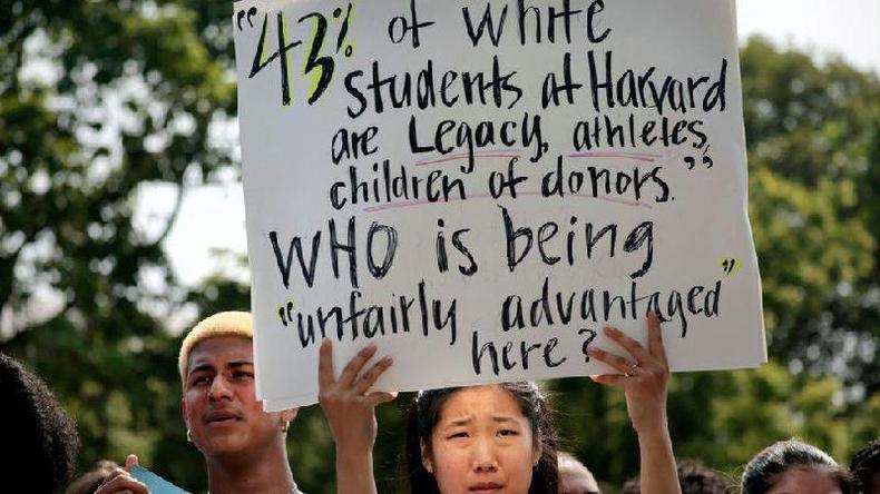Mulher com traos asiticos ao lado de jovem negro segurando cartaz com dado de que 43% dos estudantes brancos de Harvard recebem a admisso por 'legado' e de outros tipos