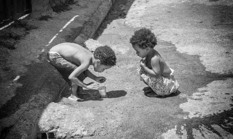 Foto em preto e branco de Enzo Daniel Amorim Santos e Eliz Elo Amorim Santos, duas crianas negras, brincando na rua