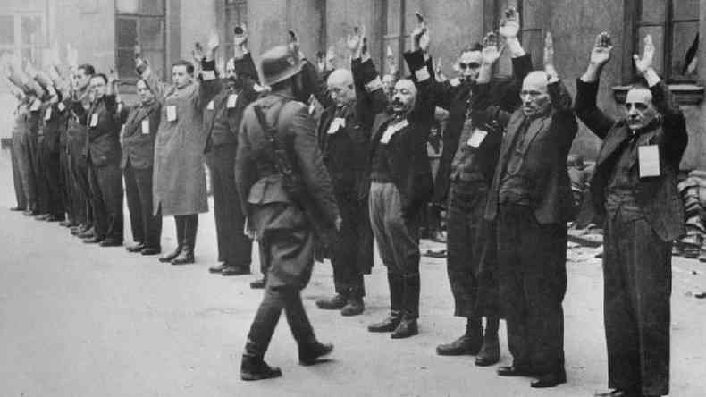 Judeus enfilerados de mos ao alto so observados por nazista