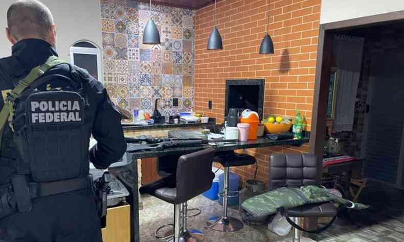 Agente federal de costas durante operao. Ele est dentro de uma casa e a sua frente tem uma mesa com alguns utenslios domsticos