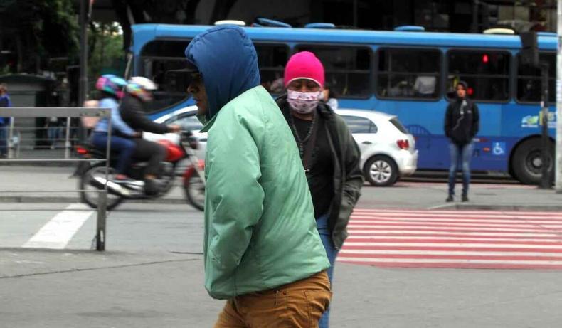 Homens usam agasalho e capuz e expresso corporal de frio andando pelo Centro de Belo Horizonte.