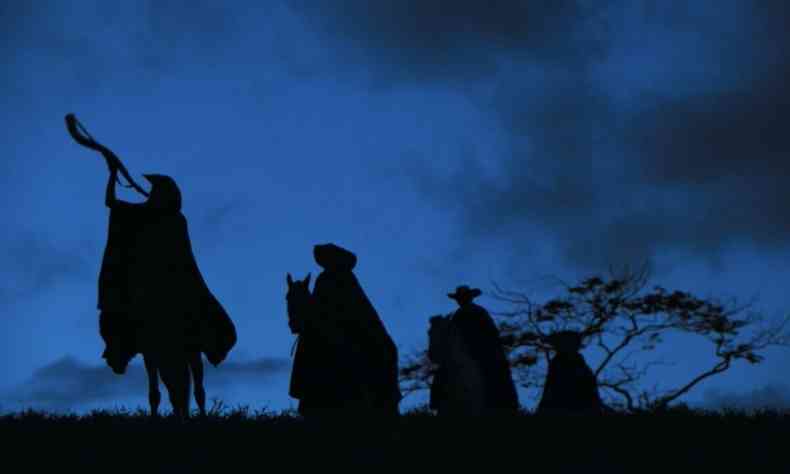 cena da novela Pantanal mostra o cu azul e sombras de vaqueiros montados em cavalos e tocando berrante