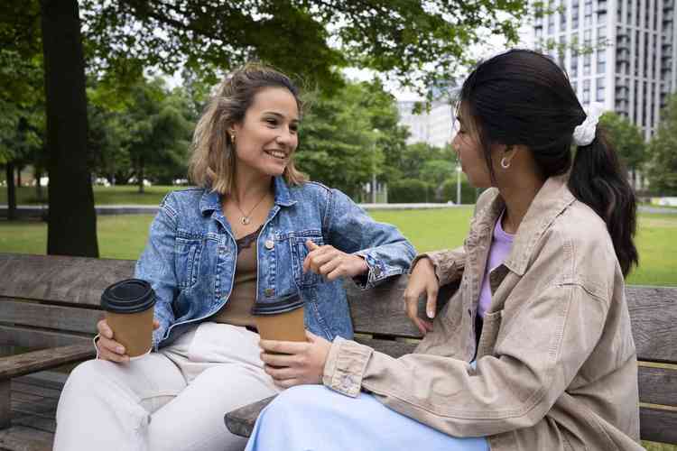 Mulheres sentadas em banco de praa conversando e tomando caf