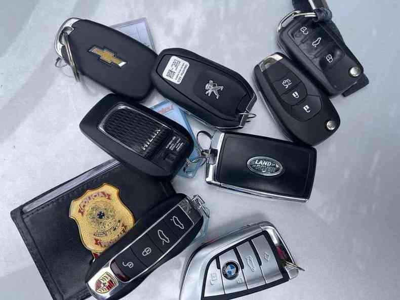 Vrias chaves de carros sobre a mesa, uma carteira da logo da PF acompanha as chaves