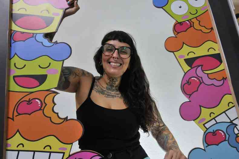 Artista Raquel Bolinho sorri no meio de grafites coloridos 