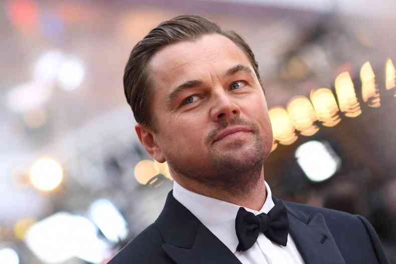 Leonardo DiCaprio usa um smoking - camisa branca, gravata borboleta preta e palet preto. Foto enquadra o ator do rosto aos ombros.