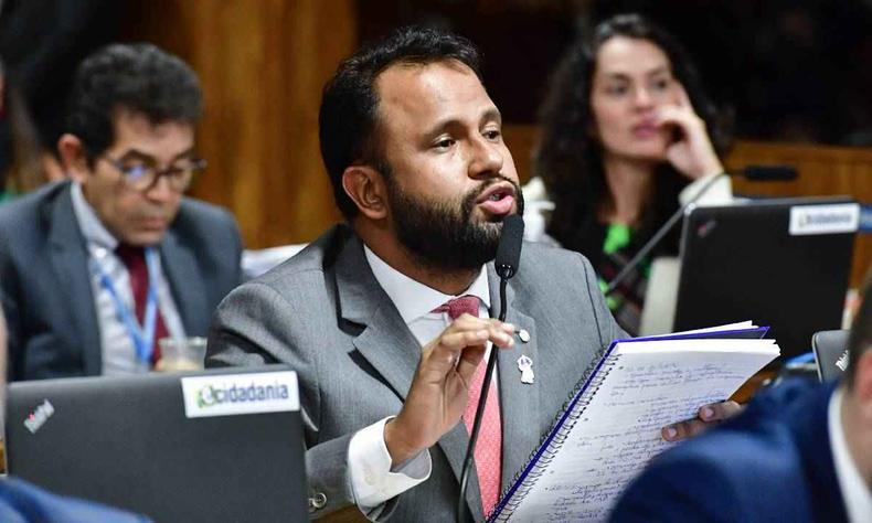 deputador Pastor Henrique Viera de terno cinza, camisa branca e gravata laranja falando eo microfone sentado  emsa na CPMI