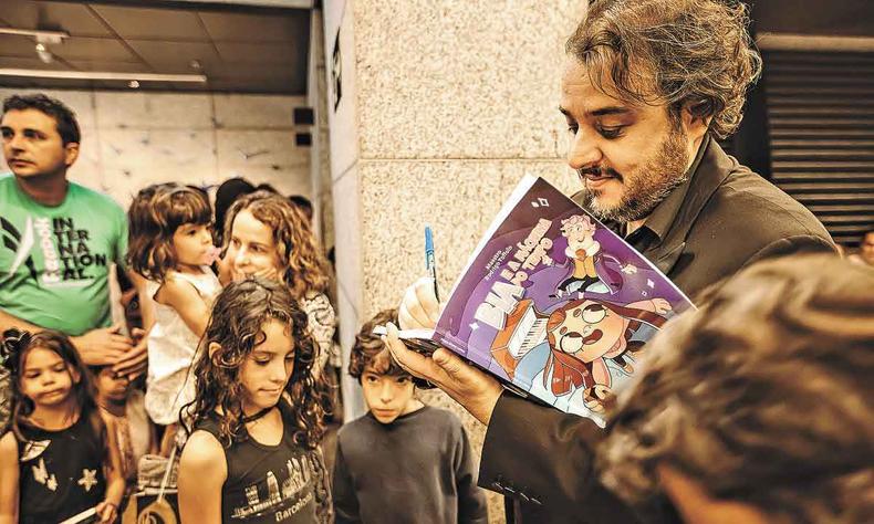 O maestro Rodrigo Toffolo fez manhã de autógrafos de seu novo livro, no domingo passado (foto: Rafa Garcia/ Divulgação) De camisa preta, Rodrigo Tofollo autografa com caneta esferográfica livro de sua autoria no saguão do Sesc Palladium, rodeado por algumas crianças