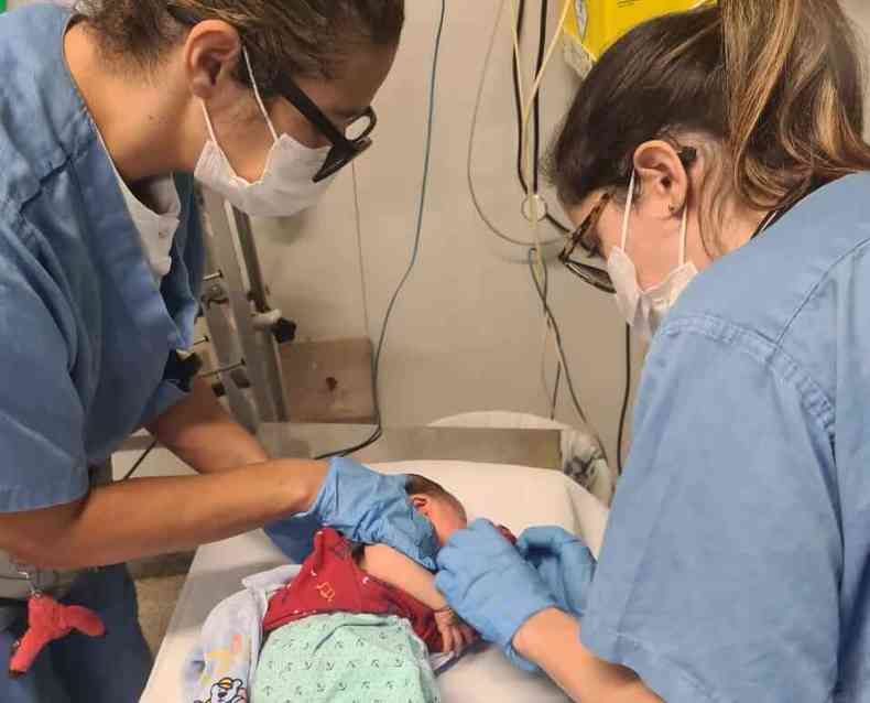 Duas profissionais de sade vestidas com uniformes hospitalares atendem beb com dificuldades para respirar