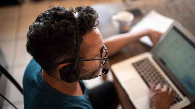Homem trabalhando de casa em frente ao laptop com fone de ouvido
