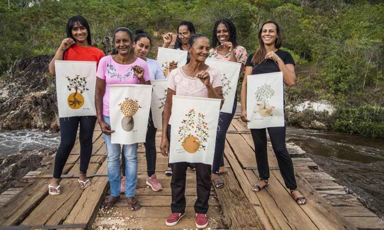 Grupo de sete mulheres em uma ponte segurando estandartes produzidos por elas 