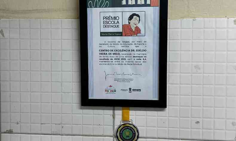 quadro com moldura preta em parede e uma medalha de prmio para a escola Dr. Edlzio em Sergipe