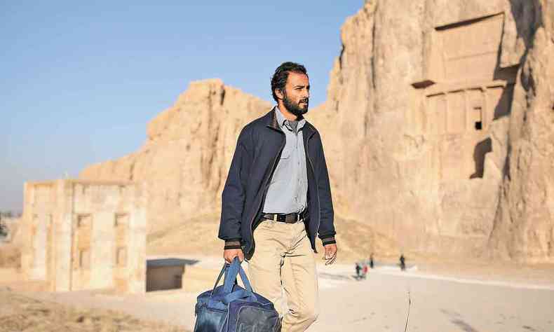 O ator Amir Jadidi caminha carregando valise em paisagem de montanha em cena de um heri 