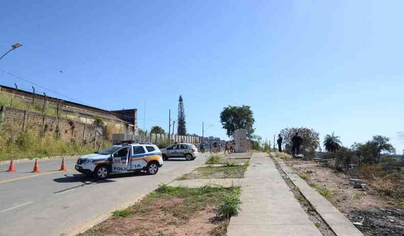 Duas viaturas paradas, e dois policias armados na frente, com um grupo de pessoas ao fundo