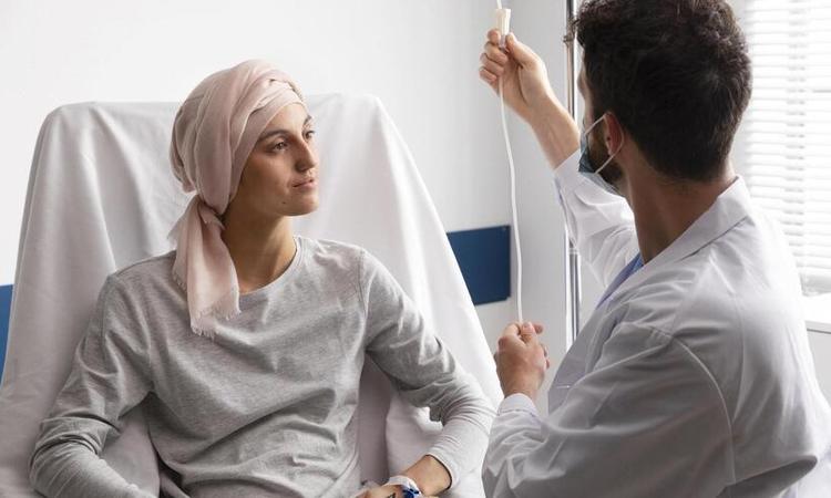 mulher com cncer, de turbante,  atendida por enfermeiro colocando soro