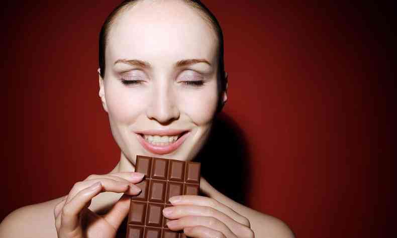 Mulher segurando uma barra de chocolate de olhos fechados e sorrindo