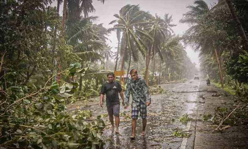 Moradores enfrentam chuva e vento forte enquanto passam por rvores arrancadas em uma estrada no centro das Filipinas(foto: Alren BERONIO / AFP)