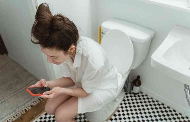 Mulher usando celular sentada no vaso sanitrio
