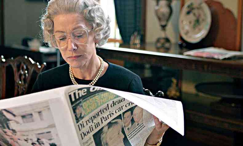 Helen Mirren no papel de Elizabeth II, envelhecida, usando culos e lendo jornal