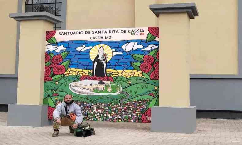 Imagem do artista Pedro Henrique Goulart Machado ao lado do mural vitral que fez para o Santuário de Santa Rita de Cássia