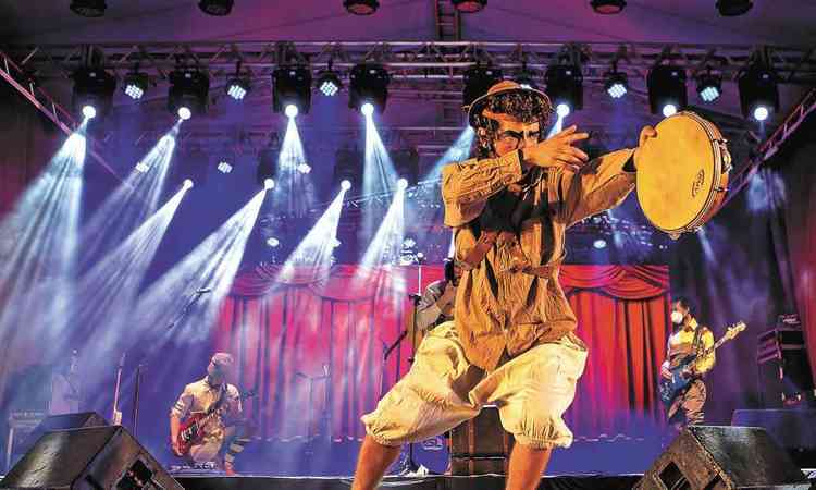 Msico toca pandeiro na frente do palco, enquanto colegas tocam violo ao fundo durante show no Festival Nacional da Cano
