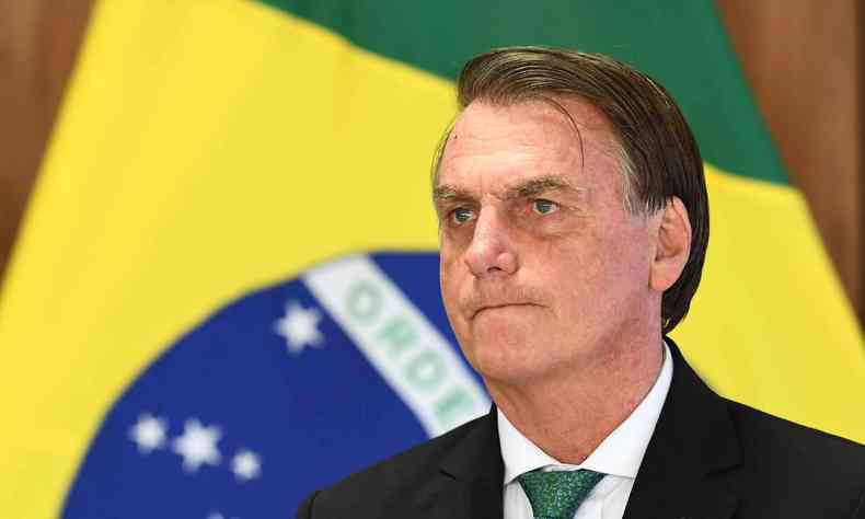 Presidente Bolsonaro em primeiro plano, com a bandeira do Brasil de fundo