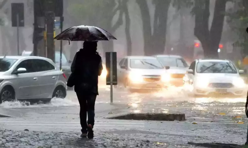 Pessoa caminha em rua alagada sob forte temporal
