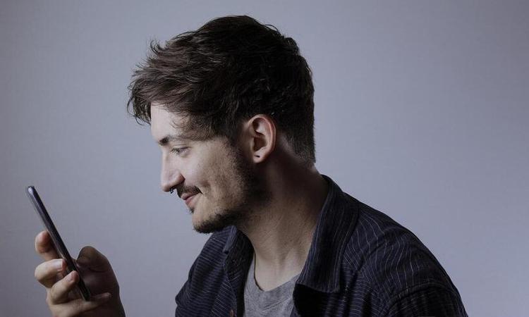 jovem de barba, piercing no nariz olhando para smartphone sorrindo