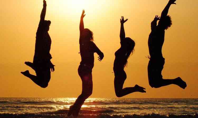 silhueta de pessoas pulando na praia ao pôr do sol
