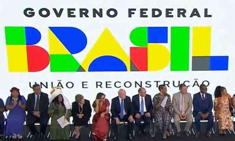 Diversas pessoas, incluindo o presidente Lula e sua esposa Janja, esto sentados em fila  frente de um painel onde se l 'Governo Federal. Brasil. Unio e Reconstruo' enquanto observam Snia Guajajara em seu discurso.