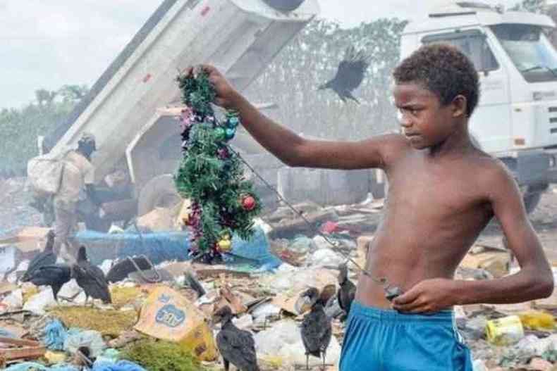 Menino segura uma árvore de Natal no lixão