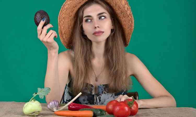 mulher diante de vrias frutas e legumes em uma mesa