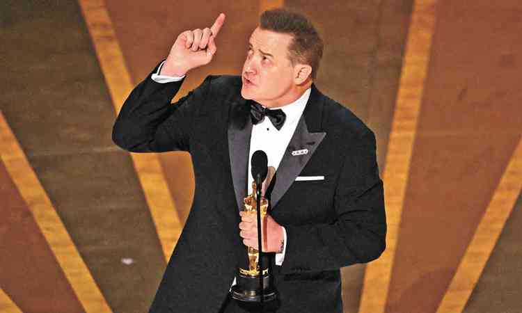 O ator Brendan Fraser olha para cima e aponta o dedo para o alto no palco do Oscar
