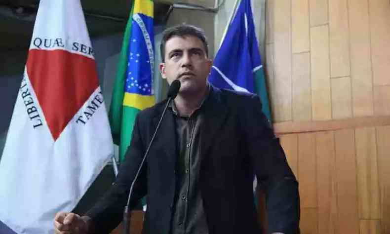Cristiano Caporezzo na ALMG com a bandeira de Minas Gerais e do Brasil ao fundo 