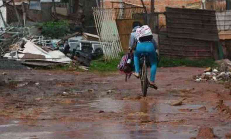 Mulher em cima de bicicleta, em rua cheia de lama e sem asfaltamento, ilustrando uma região de extrema pobreza