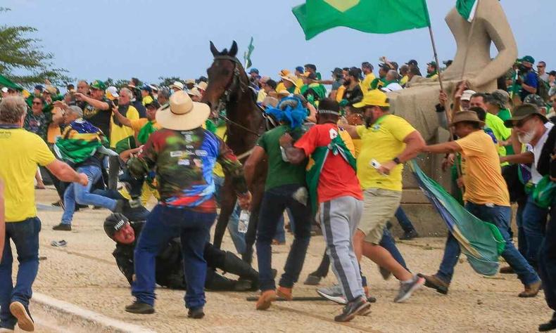 Momento em que policial  derrubado do cavalo por bolsonaristas; foto mostra policial no cho, cercado por pessoas vestidas de camisa amarela