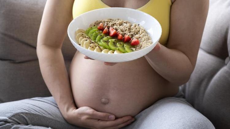 Mulher grvida comendo prato de frutas e cereal no sof