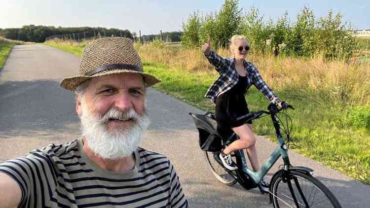 Homem tirando selfie com mulher ao fundo pedalando enquanto sorriem