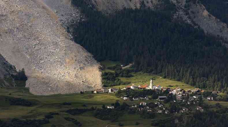 Foto area mostra enorme quantidade de pedras deslizadas, com vilarejo embaixo