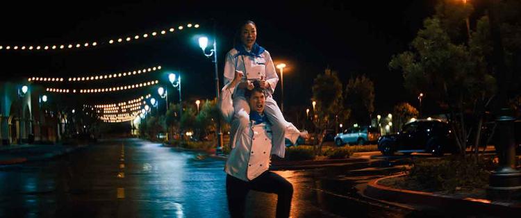 Cena de 'Tudo em todo lugar ao mesmo tempo' em que Michelle Yeoh e chef correm pela rua; ela sentada nos ombros dele