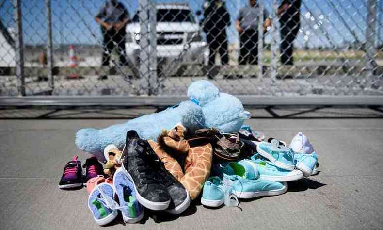 Brinquedos e sapatinhos de crianças, separadas dos pais na fronteira, abandonados no portão de entrada de Tornillo, no estado do Texas. Em pé, no fundo da imagem, seguranças do governo estadunidense(foto: Brendan Smialowski/AFP)