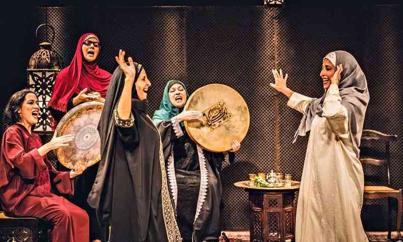 Cinco atrizes do grupo Amok de Teatro, com roupas rabes, danam e tocam instrumentos de percusso semelhantes a bandejas. Ao fundo v-se mesinha com ch