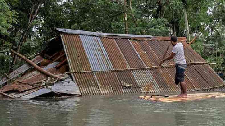 Homem navega perto de casa submersa pela gua de enchente em Bangladesh