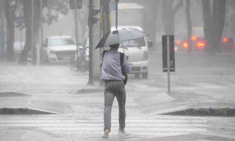 Homem caminha com guarda-chuva em rua de BH