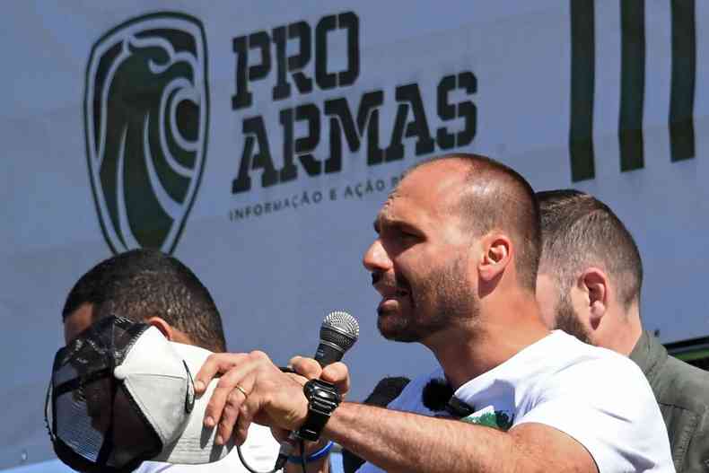 Eduardo BOlsonaro fala ao microfone; ao fundo um painel com os dizeres 'pr-armas' 