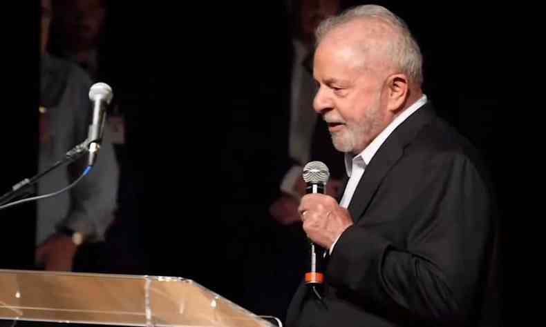 Lula de lado, com palet preto e camisa branca, falando com um microfone na mo